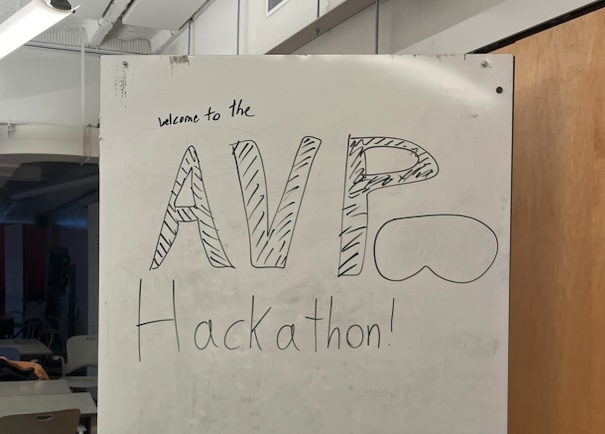 Whiteboard with a hand-drawn Welcome to the AVP Hackathon sign, the P doubling as a Vision Pro