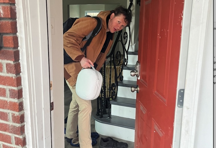 Hackathon attendee arriving in a doorway, carrying a Vision Pro in its white case