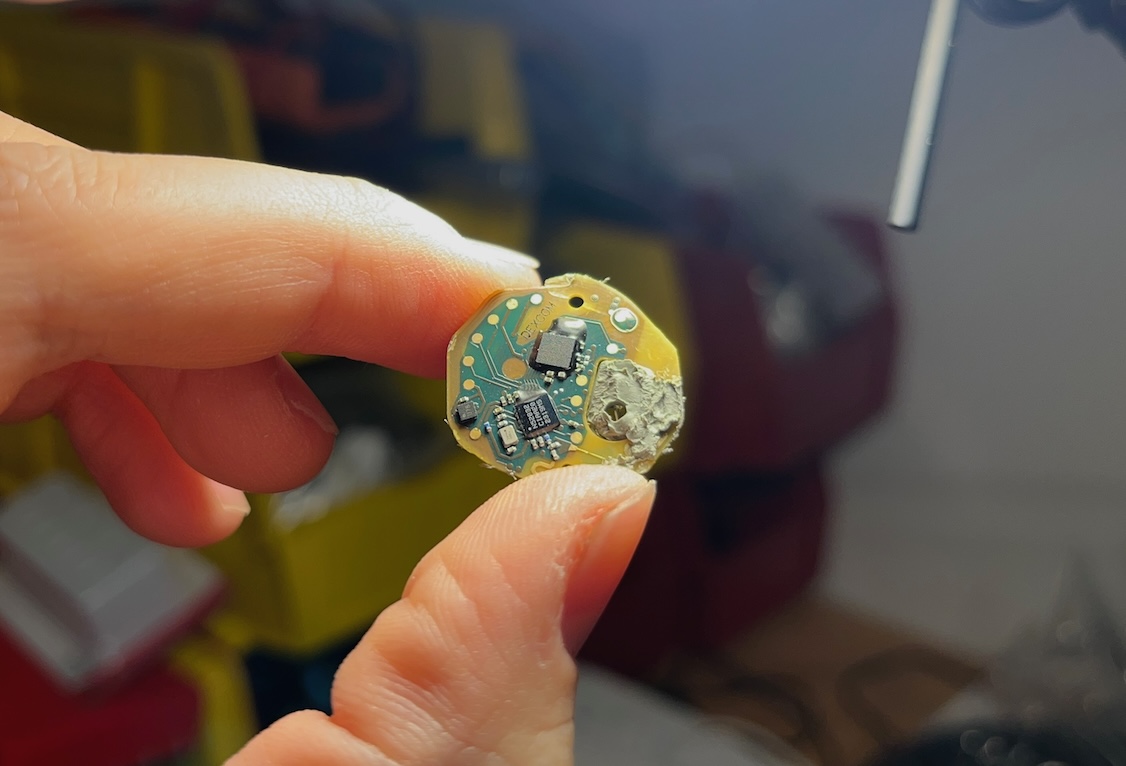 Fingers holding the thin round Stelo circuit board freed from its rubber casing