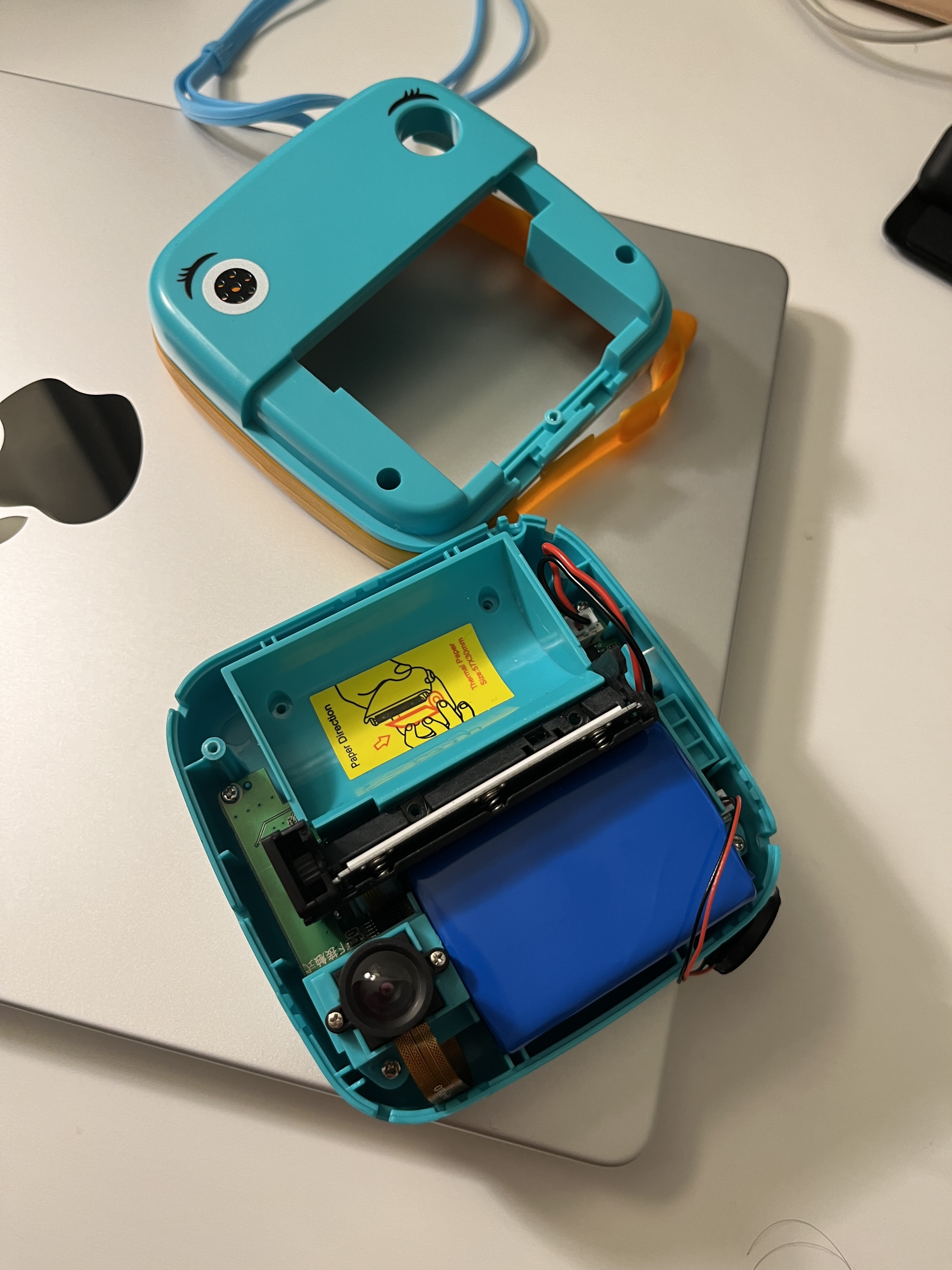 Teal dinosaur toy camera opened up, showing thermal printer, camera lens, and blue battery pack inside