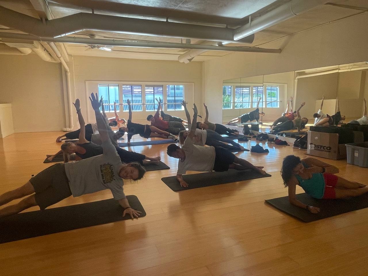 Pilates class holding side planks on mats in a sunny mirrored studio