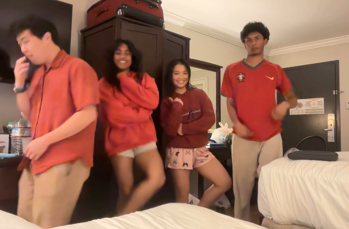 Four friends in matching red shirts dancing together in a hotel room