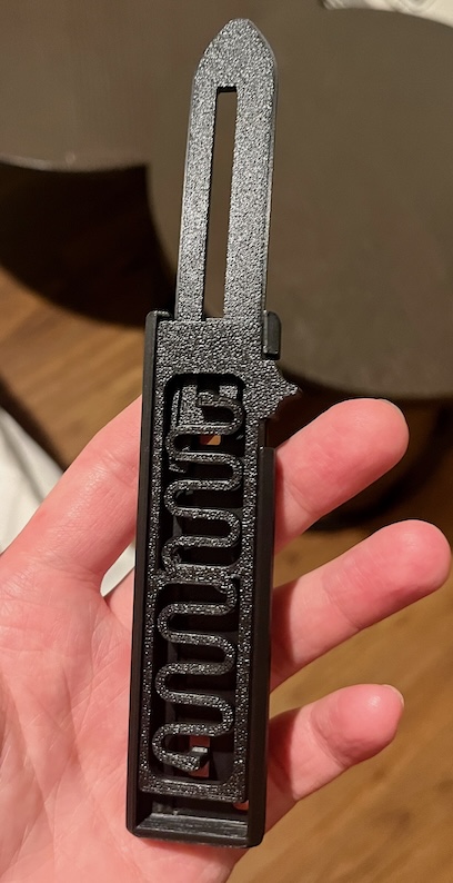 Black 3D printed retractable knife with a springy serpentine flexure in the handle, held in one hand