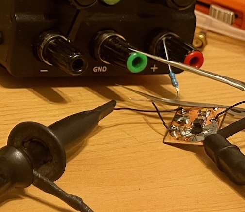 Bench power supply feeding the breakout board through an in-line resistor, with a scope probe attached