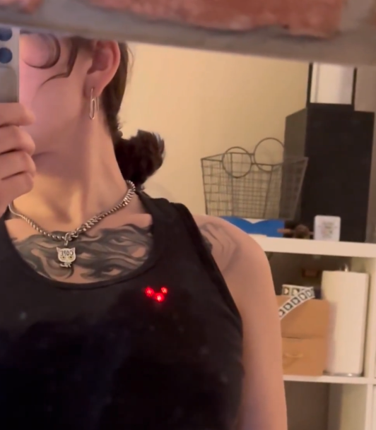 Mirror selfie with two red LEDs glowing through a black tank top from the wearable EKG heart visualizer