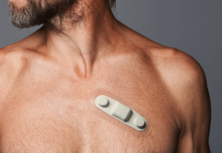 Compact all-in-one wearable EKG patch monitor adhered across a man's chest