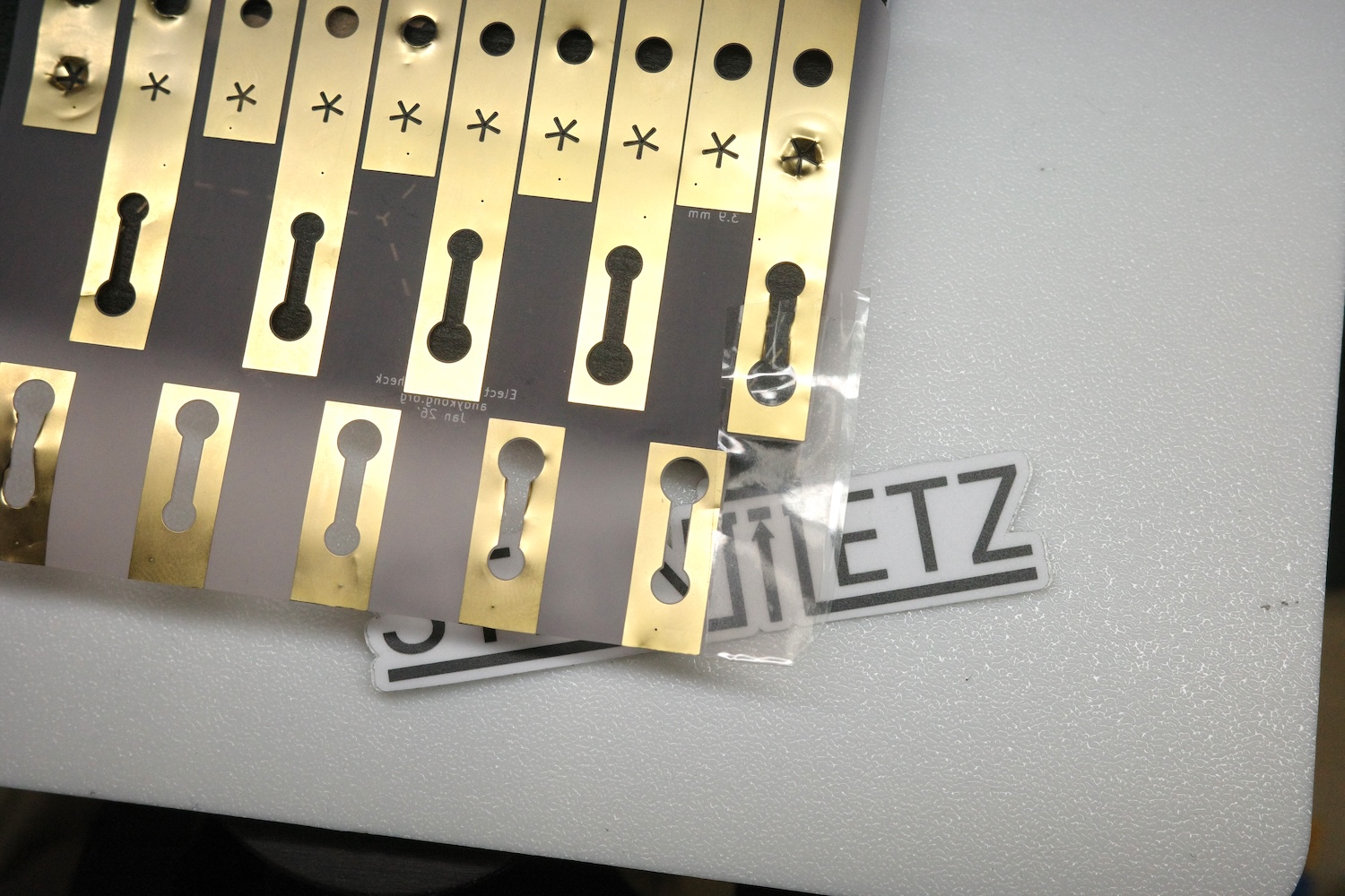Manufactured clear flex PCB with exposed gold strips and keyhole cutouts on a translucent frosted substrate
