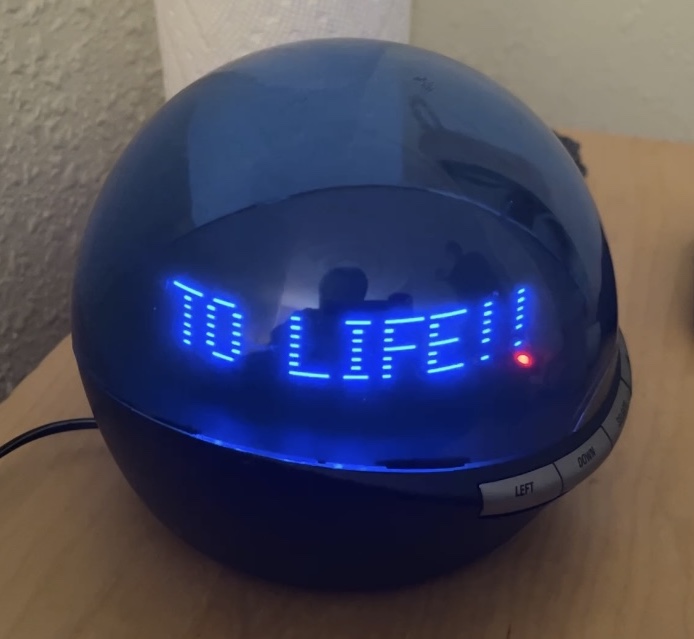 Reassembled Infoglobe with its blue dome displaying TO LIFE!! in glowing dot-matrix letters
