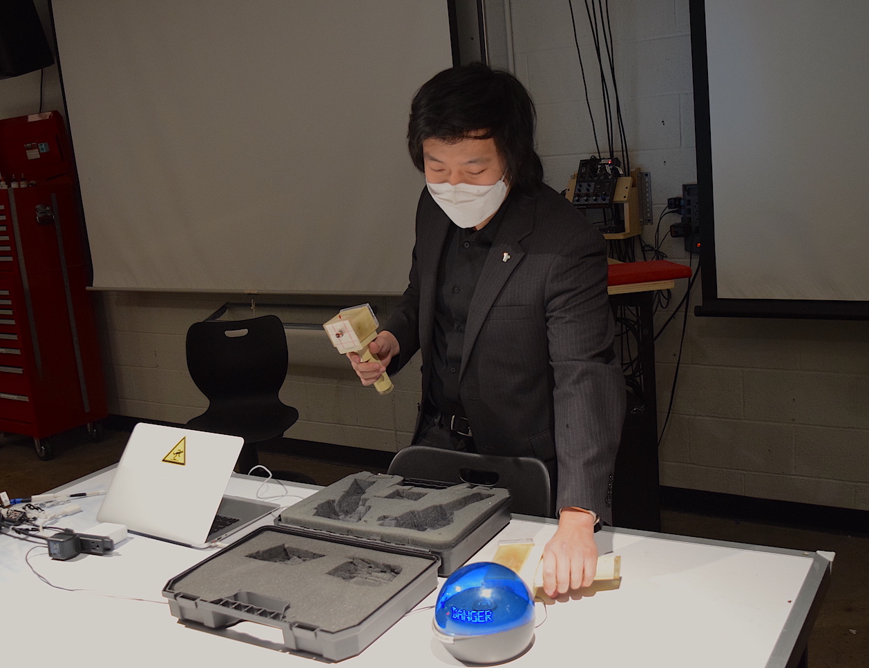 Andy in a suit and mask demonstrating the Meiger Counter beside its open carrying case