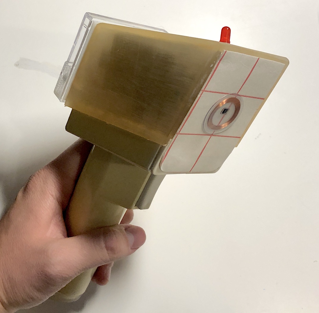 Hand holding the translucent amber Meiger Counter, showing the copper coil antenna behind its crosshair face