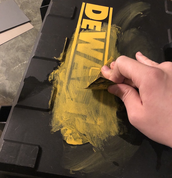 Hand scrubbing yellow paint off the embossed DeWalt logo on the black carrying case