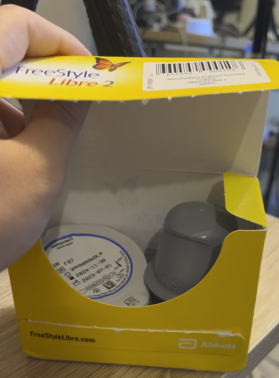 Opened yellow FreeStyle Libre 2 box showing the sealed sensor cup and grey applicator inside