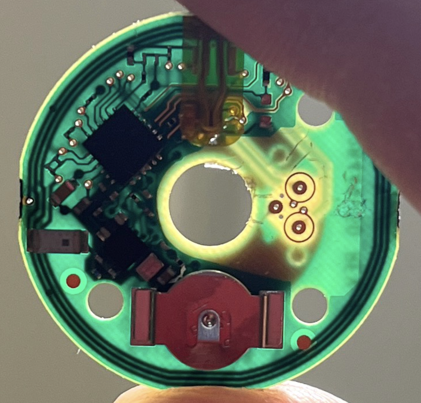 Sensor PCB held against the light, revealing guard ring inputs and the copper NFC coil looping the board