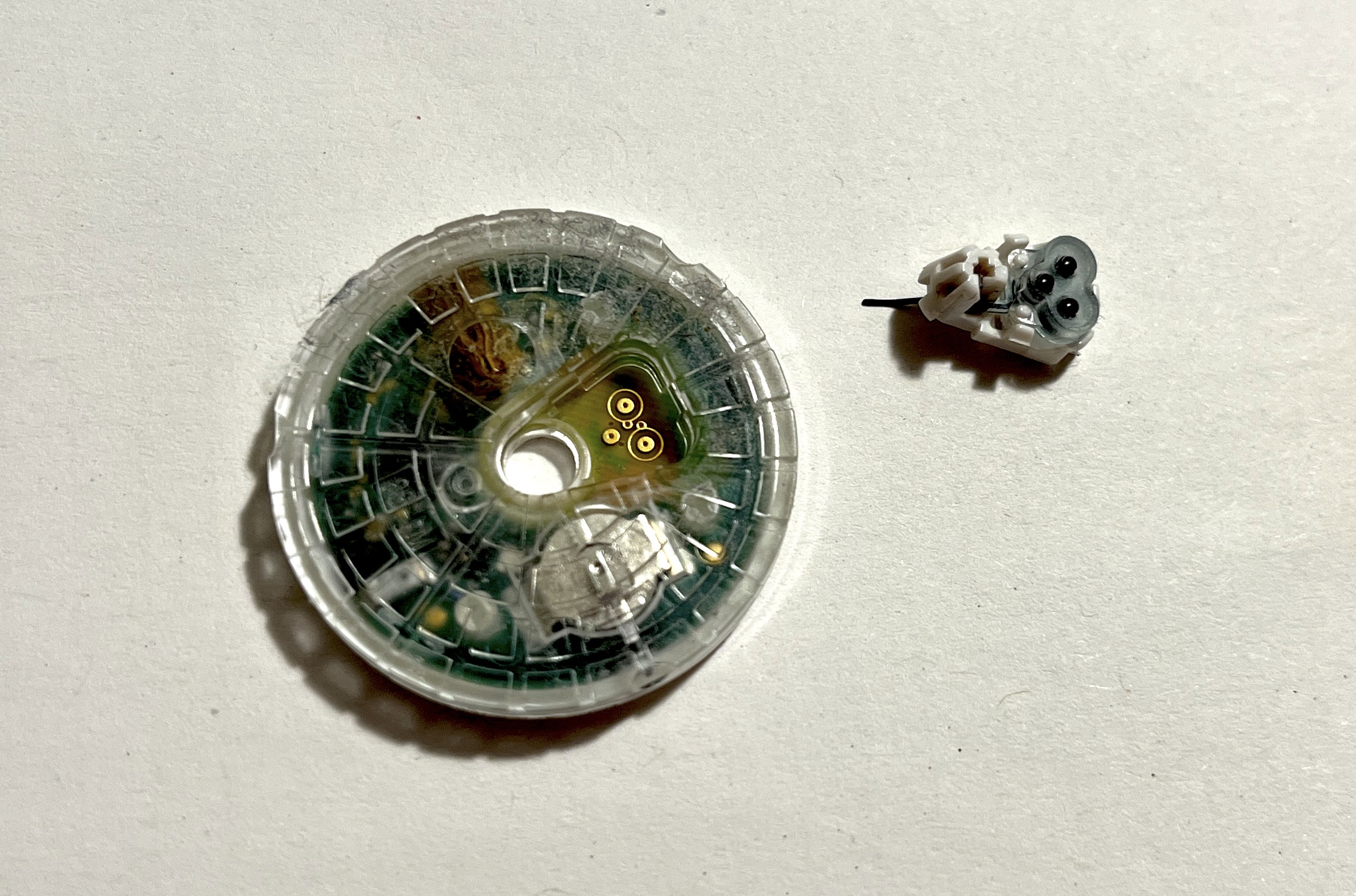 Translucent sensor disc next to the tiny removed needle assembly with its three black squishy contacts
