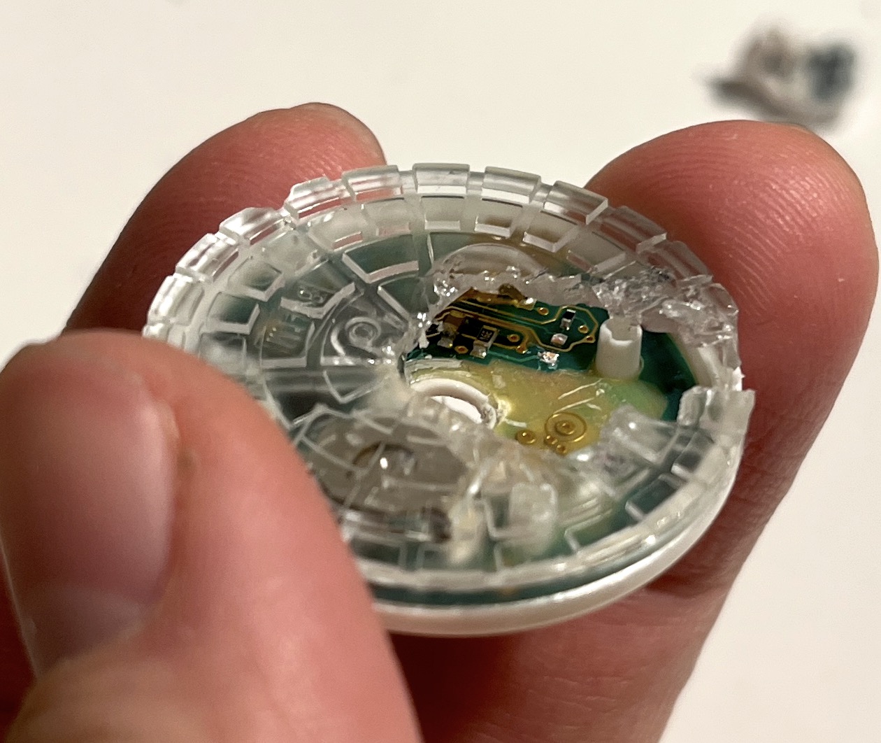 Fingers holding the sensor with its clear plastic housing cracked open, exposing part of the green PCB