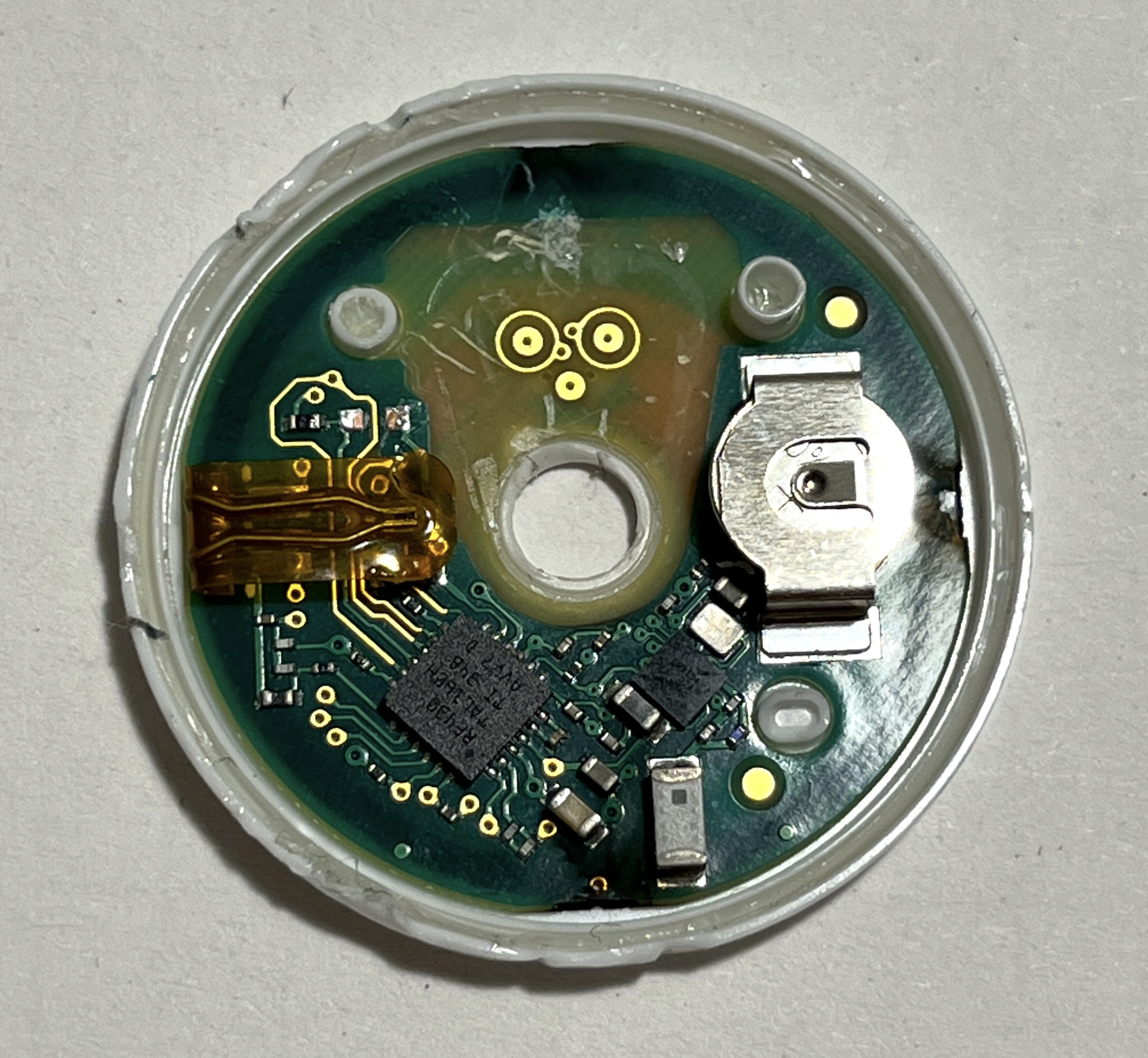 Sensor PCB freed of plastic, showing the coin cell battery clip, chips, and gold needle contact pads