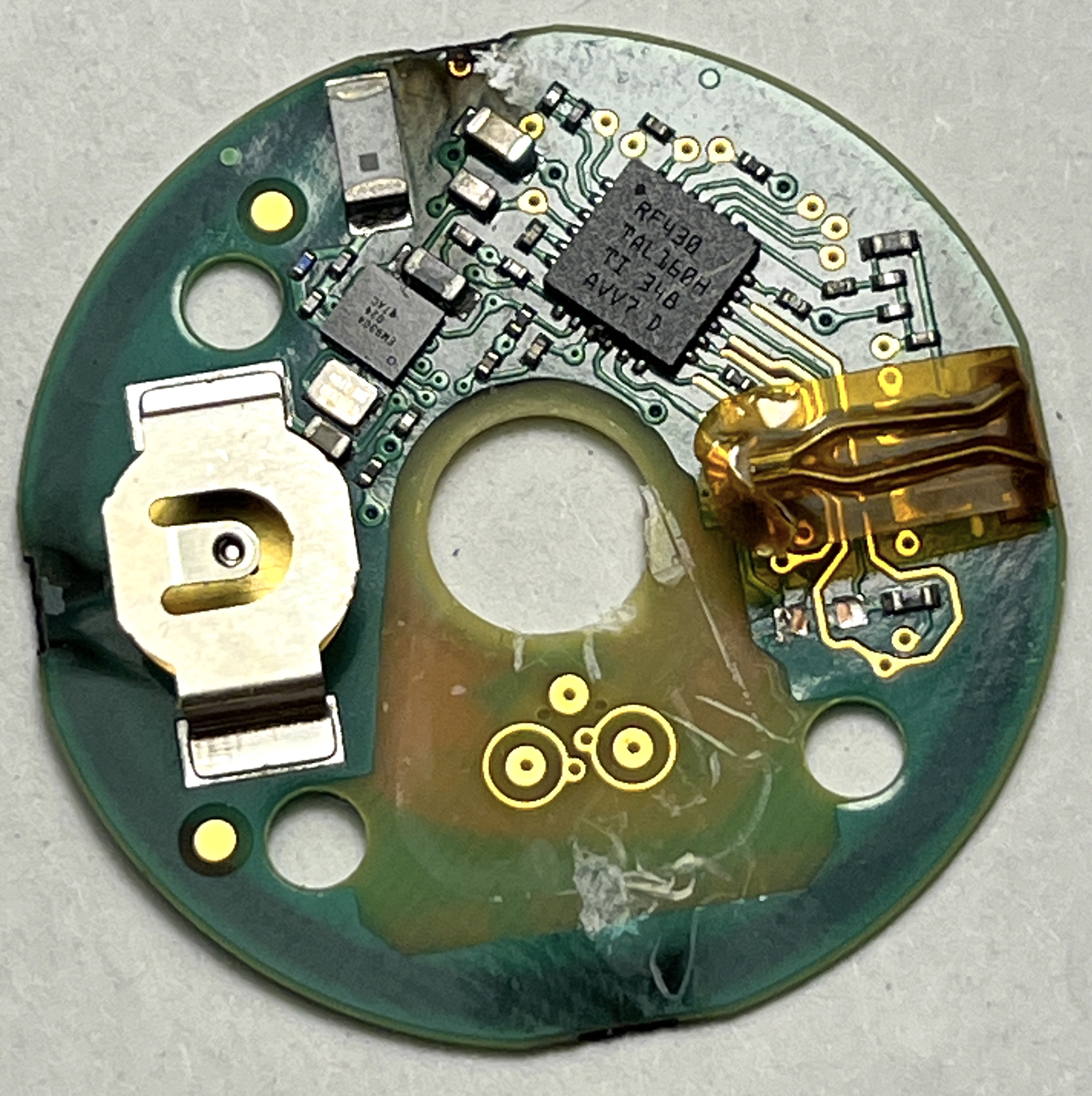 Close-up of the round PCB with the TI RF430 NFC chip, battery clip, and kapton-taped needle contacts