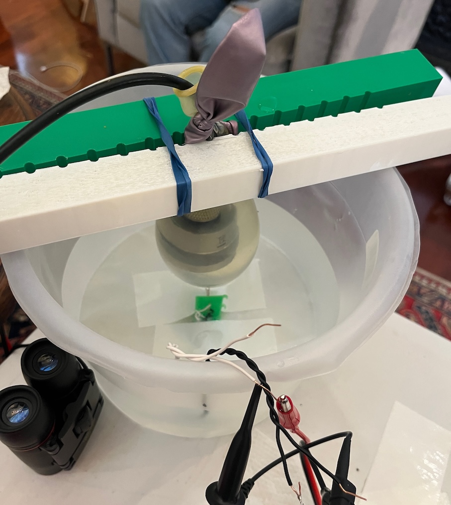 Ultrasonic transducer suspended in a water bath with test leads and a receiving element below it