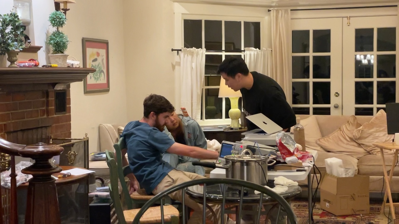 Three hackers working late at night around a cluttered living-room lab bench