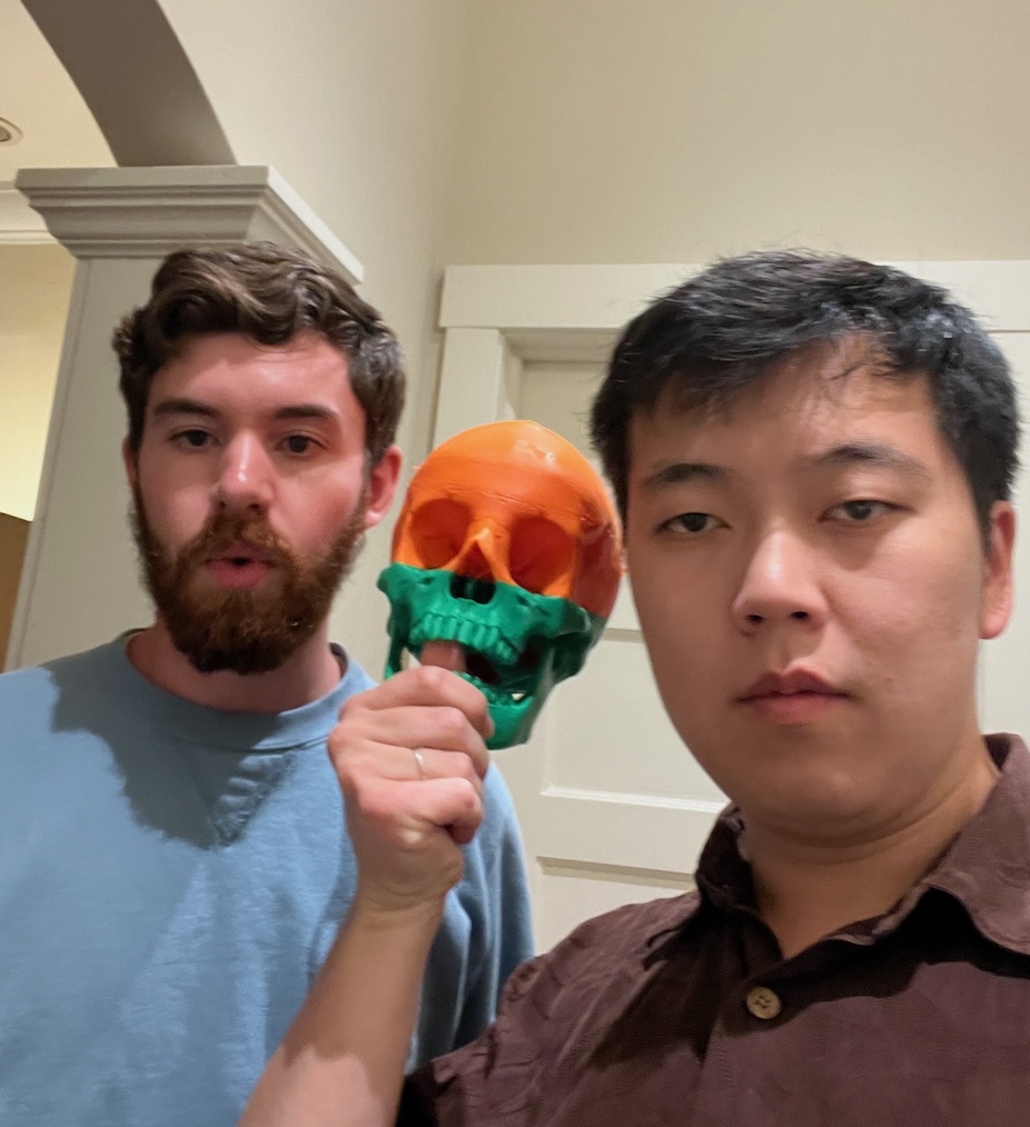 Two of us posing for a selfie holding an orange-and-green 3D-printed skull between us