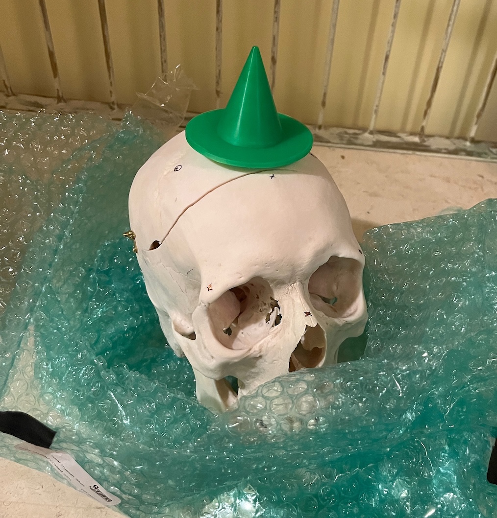 Human skull wearing a green 3D-printed witch hat, sitting on bubble wrap