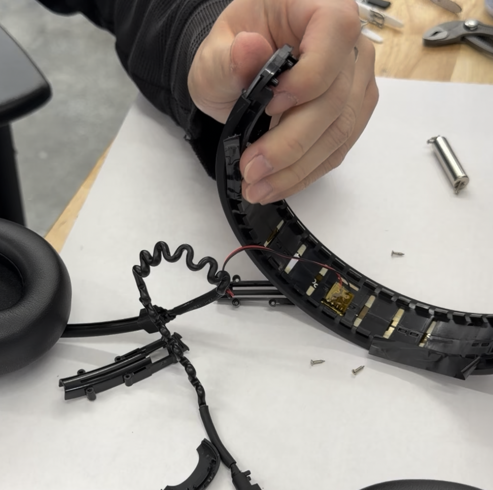 Hands pulling the headband frame apart, with the coiled interconnect cable and inner rails exposed