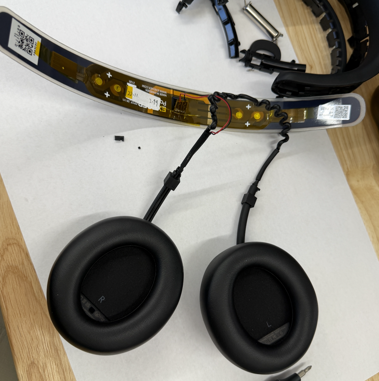 Freed PowerFoyle solar cell strip with its flex circuit and QR labels, next to the two detached earcups