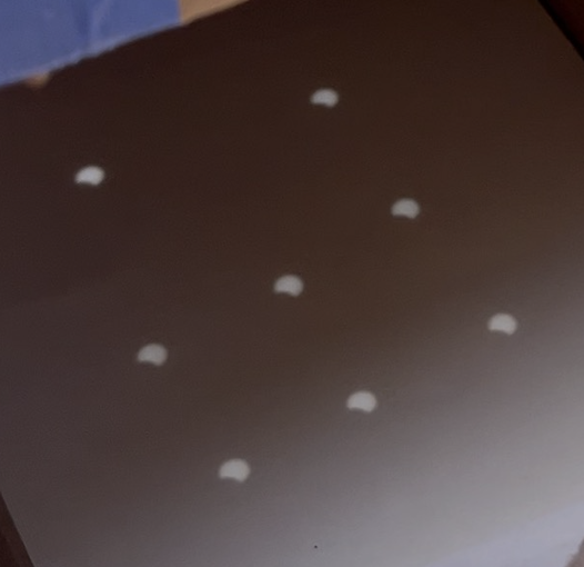 Crescent-shaped eclipse shadows projected as a grid of spots on a dark surface